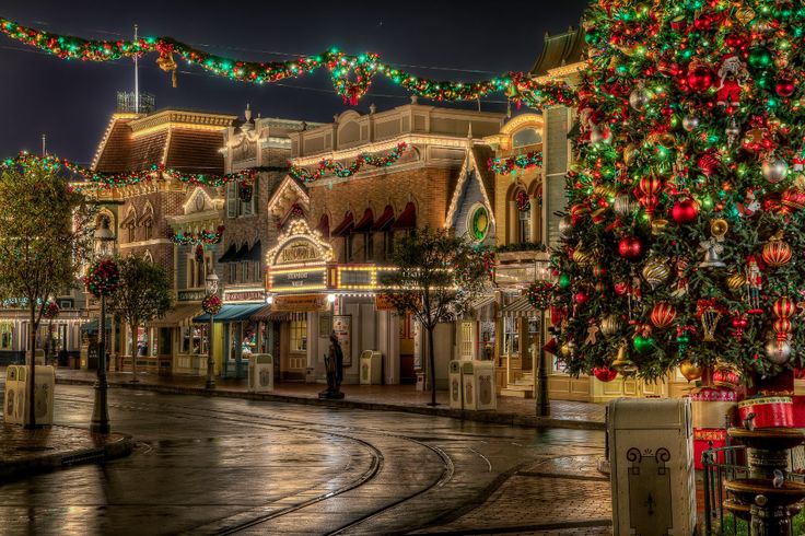 a christmas tree is lit up in the middle of a city street with buildings and lights all around it