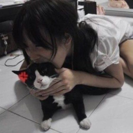 a woman laying on the floor holding a black and white cat with her face close to her chest