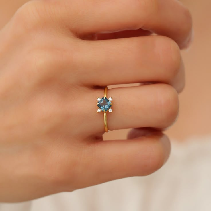 a woman's hand wearing a gold ring with a blue topazte stone