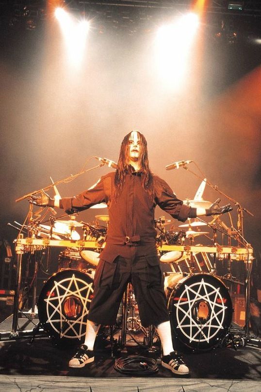 a man with long hair standing in front of a drum set and drums on stage