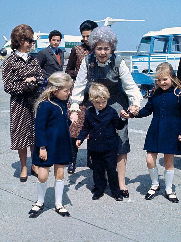 an older woman and two small children are standing in front of some other people on the tarmac