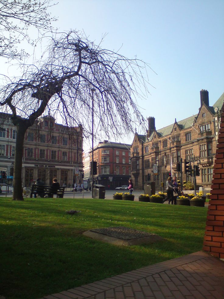 people are sitting on benches in the middle of a grassy area next to some buildings