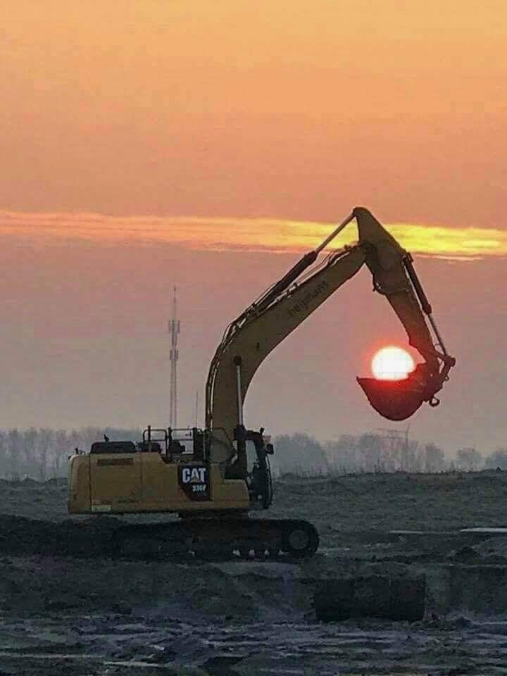 an excavator is setting on the ground with the sun in the background