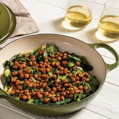 a green pot filled with food next to two glasses of wine on top of a white table