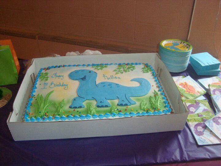 a birthday cake with a blue dinosaur on it sitting in front of a purple tablecloth