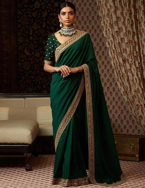 a woman wearing a green sari with gold detailing on the neck and shoulder, standing in