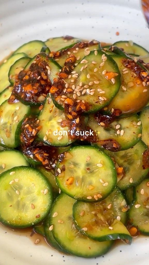 a white plate topped with sliced cucumbers covered in sesame seeds and seasoning