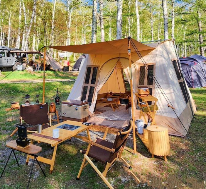 an outdoor tent set up in the woods with chairs and tables next to it, surrounded by camping equipment