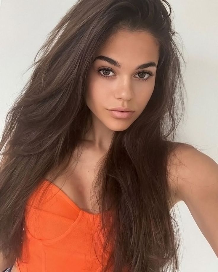 a woman with long brown hair wearing an orange top