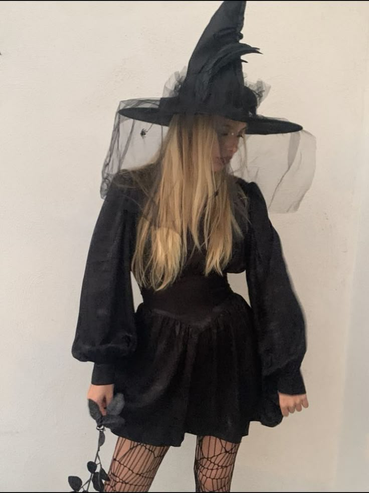 a woman in a black dress and witch hat is standing with her hands on her hips