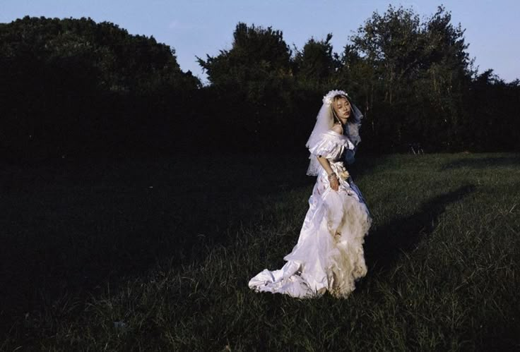 a woman in a wedding dress is walking through the grass