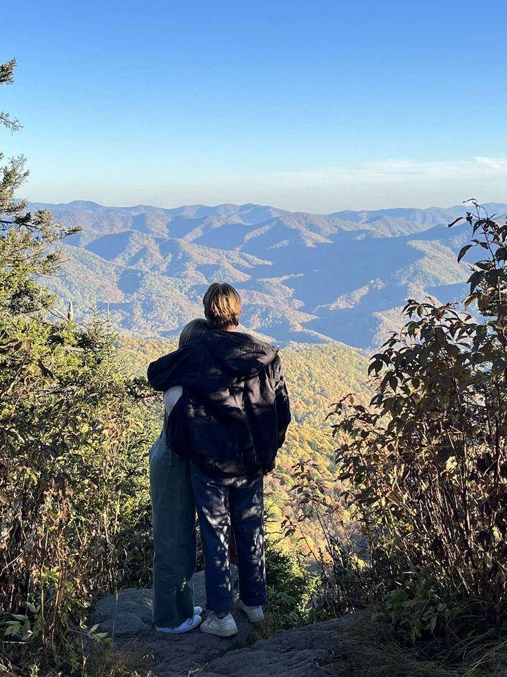 two people standing on top of a mountain looking at the mountains