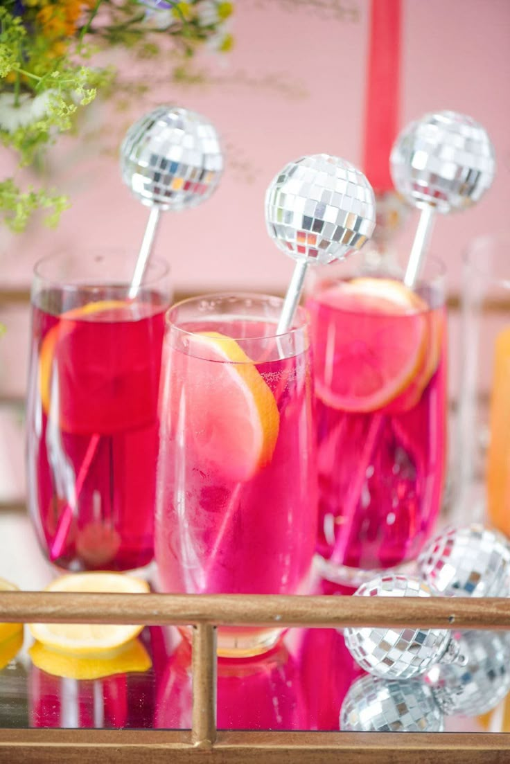 three glasses filled with pink liquid and topped with silver disco ball toppers sitting on a tray