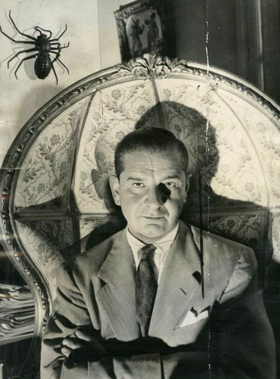 black and white photograph of man in suit with spider on the wall behind him,