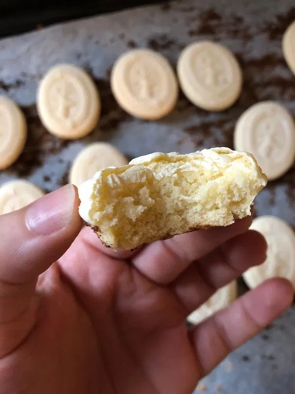 someone holding up a half eaten cookie in front of some cookies on a baking sheet