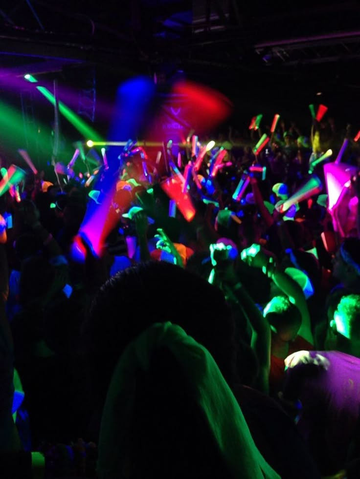 a large group of people in a dark room with colored lights on their hands and arms