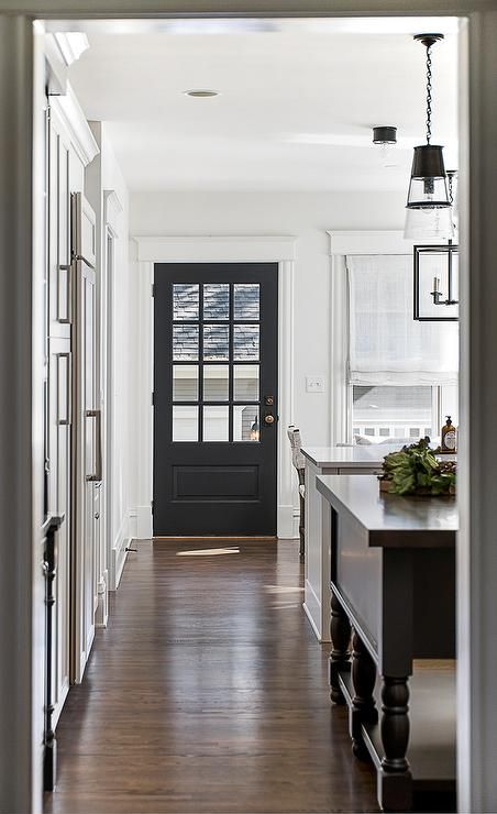 an open door leading to a kitchen and dining room with dark wood floors, white walls and black doors