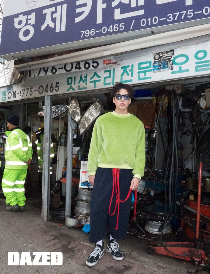 a woman standing in front of a store wearing sunglasses and a green sweater with the words dazed written on it