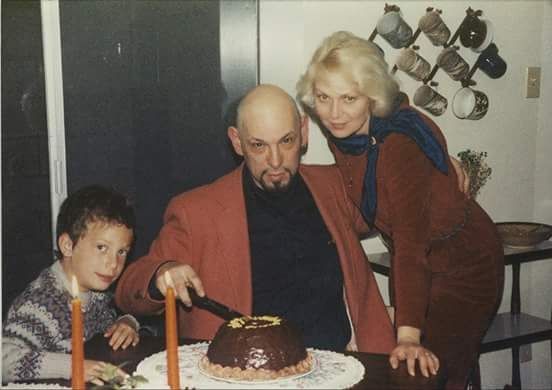 a man and woman cutting a chocolate cake with two small children sitting next to them