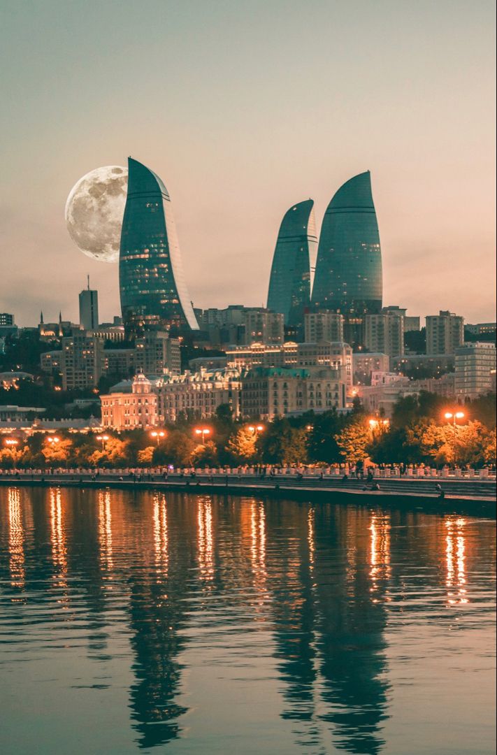 the full moon is reflected in the water next to some tall buildings and skyscrapers