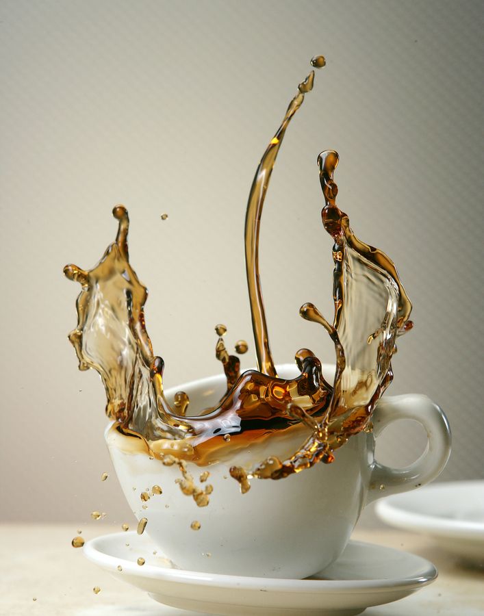 coffee splashing into a white cup on top of a saucer and another plate