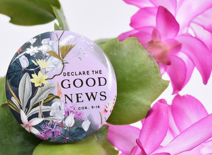 a button with flowers on it sitting next to some pink flowers and green leafy branches