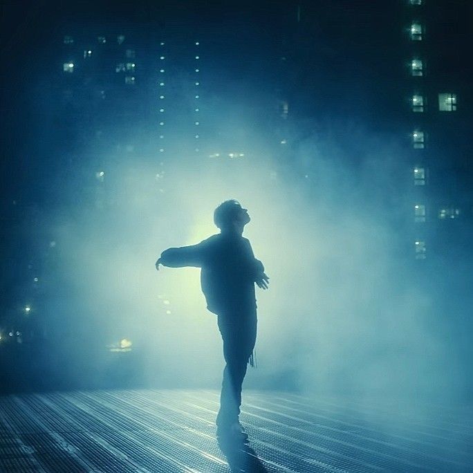 a man standing in the middle of a foggy street at night with his arms outstretched