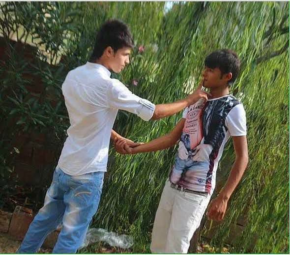 two young men standing next to each other in front of some tall green grass and plants