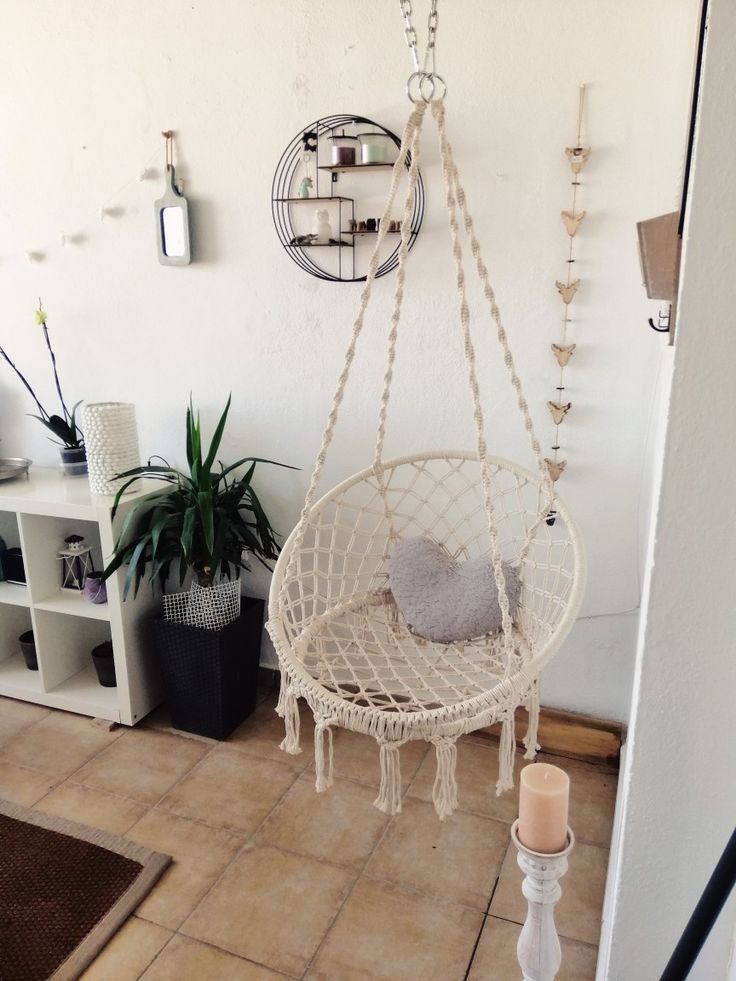 a white hanging chair in the corner of a room with potted plants and candles