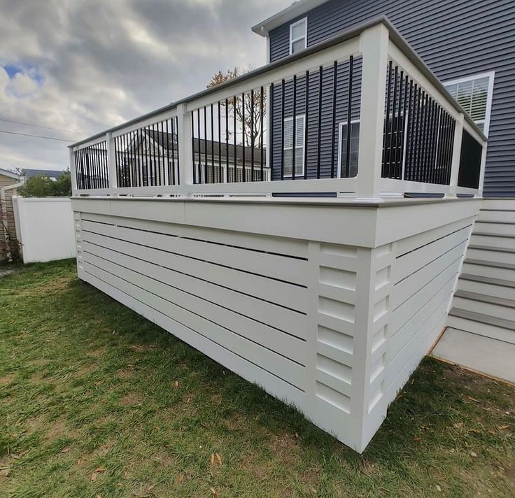 a large white deck in front of a house with windows and railings on the side