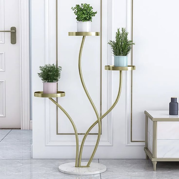 three potted plants sitting on top of two gold stands in front of a white door