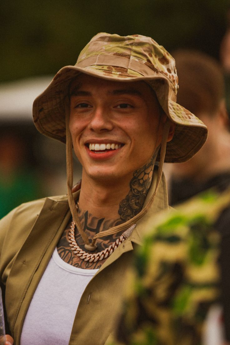 a man with tattoos wearing a hat and smiling at the camera while standing in front of other people