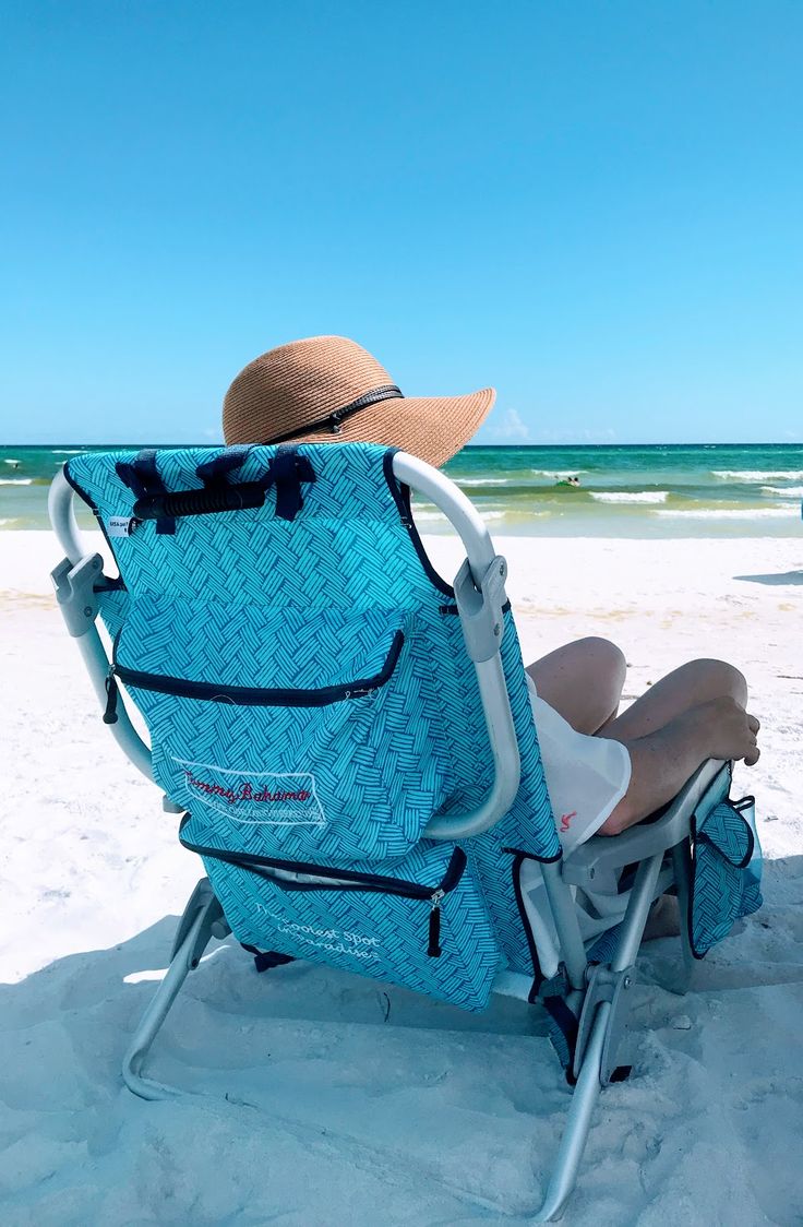 a person sitting in a beach chair on the sand with a hat on their head