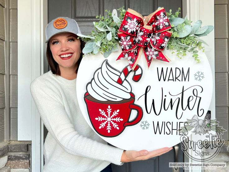 a woman holding up a sign that says warm winter wishes with a cup of coffee