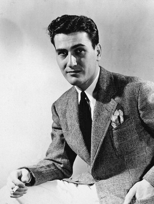 an old photo of a man in a suit and tie sitting on a chair with his hands folded