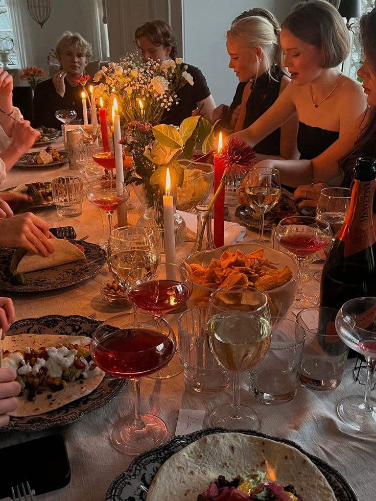 a group of people sitting around a dinner table with food and wine glasses on it