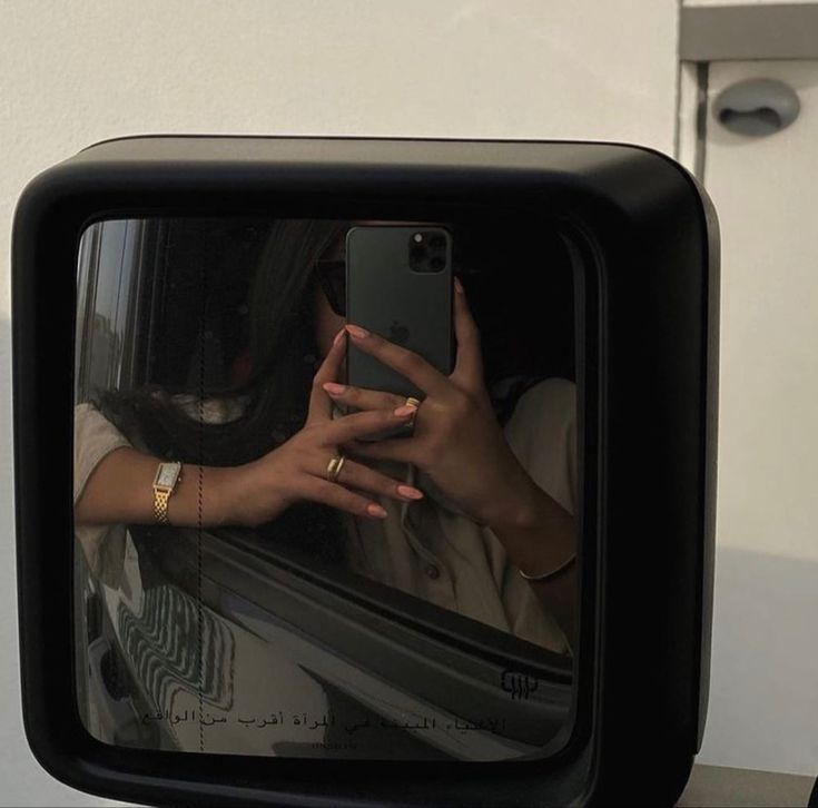 a woman taking a selfie with her cell phone in front of a car mirror