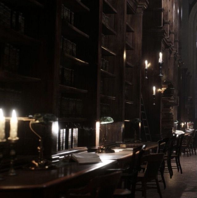 a dimly lit room filled with lots of tables and chairs next to tall bookshelves