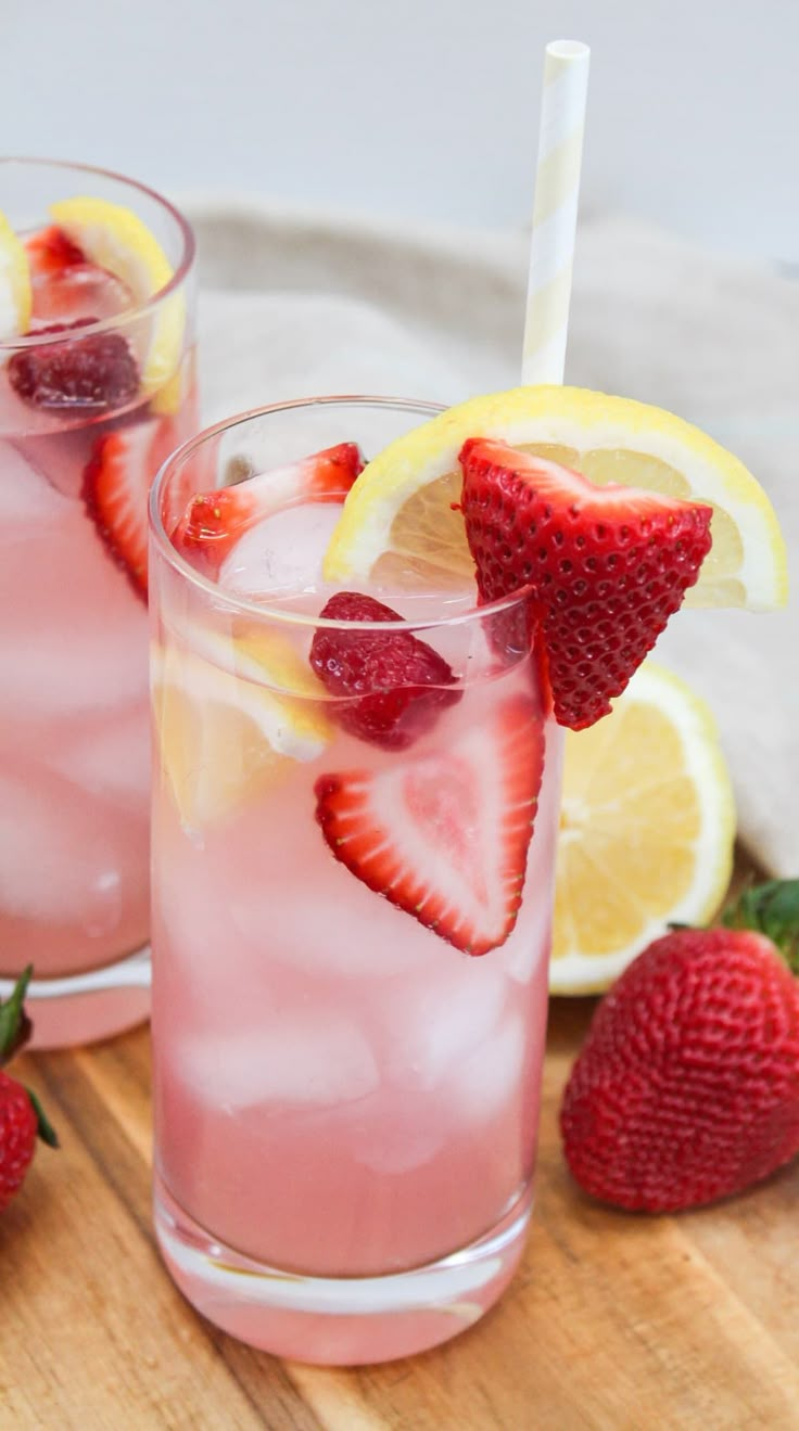 two glasses filled with pink lemonade and strawberries on top of a cutting board