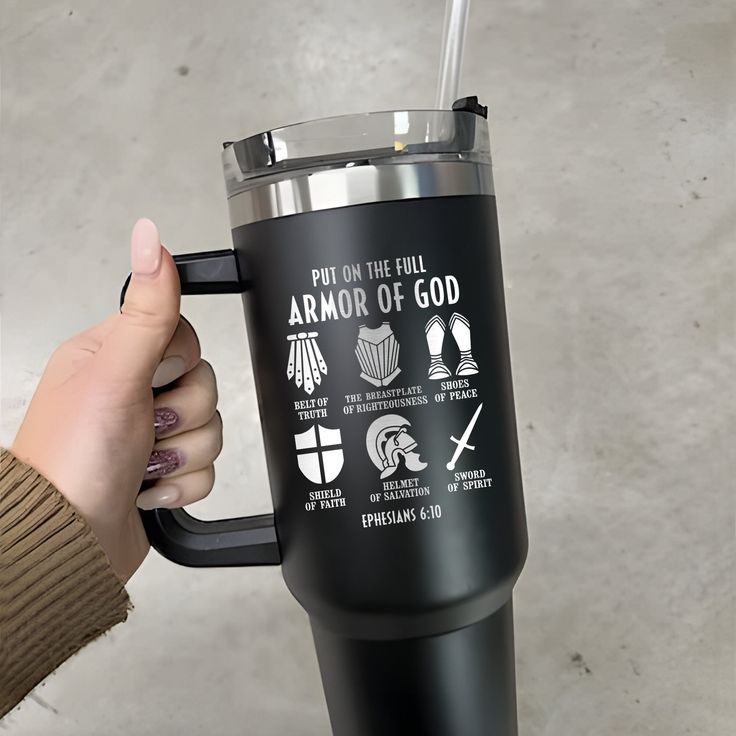 a person holding a travel mug with the words armor of god on it and symbols