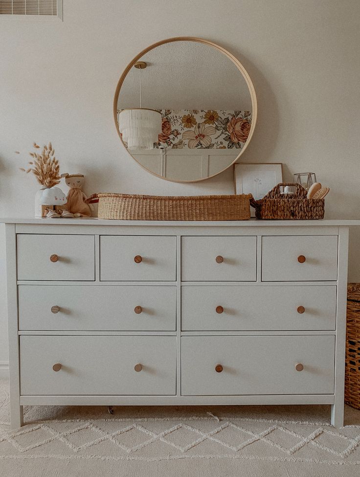 a white dresser with drawers and a round mirror above it on top of the dresser