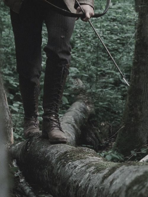 black and white photograph of a man with an arrow on a fallen tree in the woods