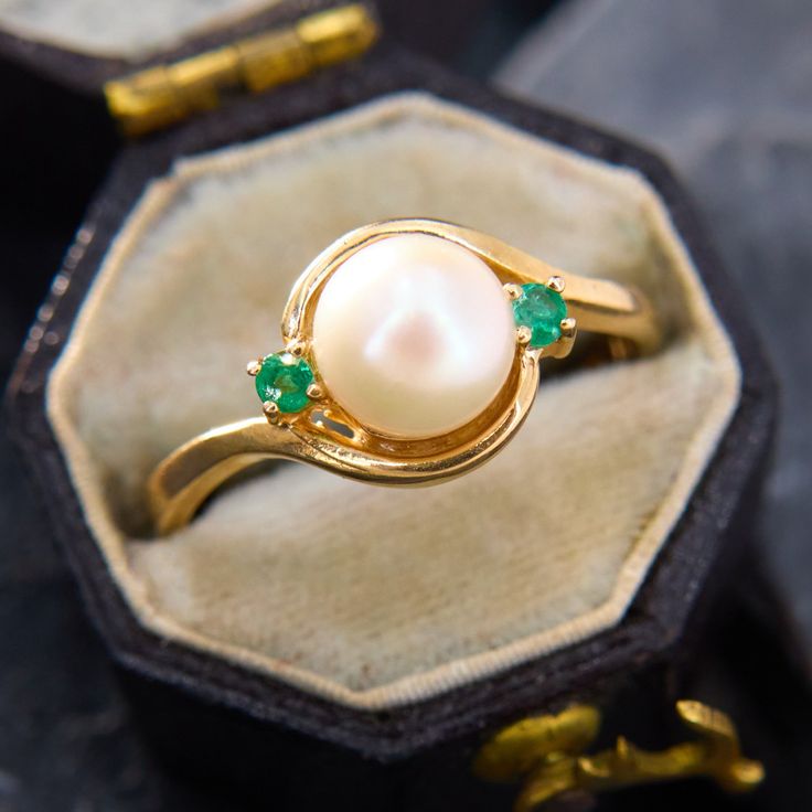 a close up of a ring with pearls and emeralds on it in a box