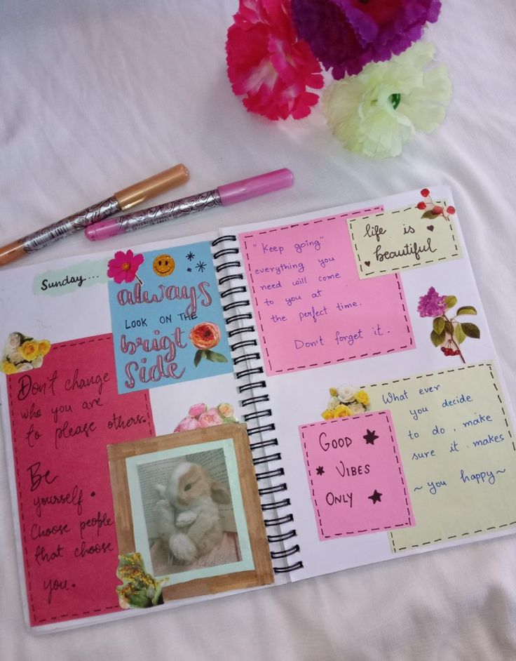 an open notebook with pictures and writing on it, next to a flower vase filled with flowers