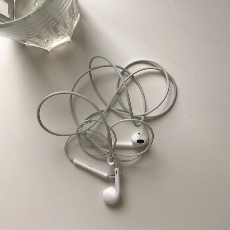 there are headphones on the table next to a water bottle and glass vase with liquid in it