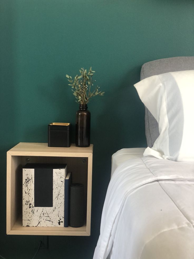 a nightstand with two books and a plant on it next to a bed in a green room