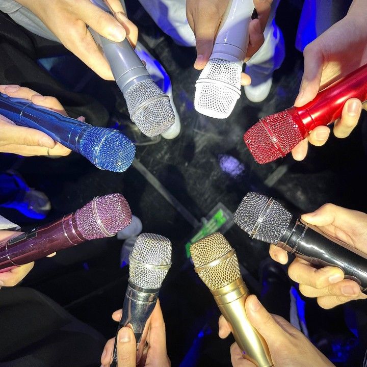 a group of people holding microphones in a circle with their hands on top of each other