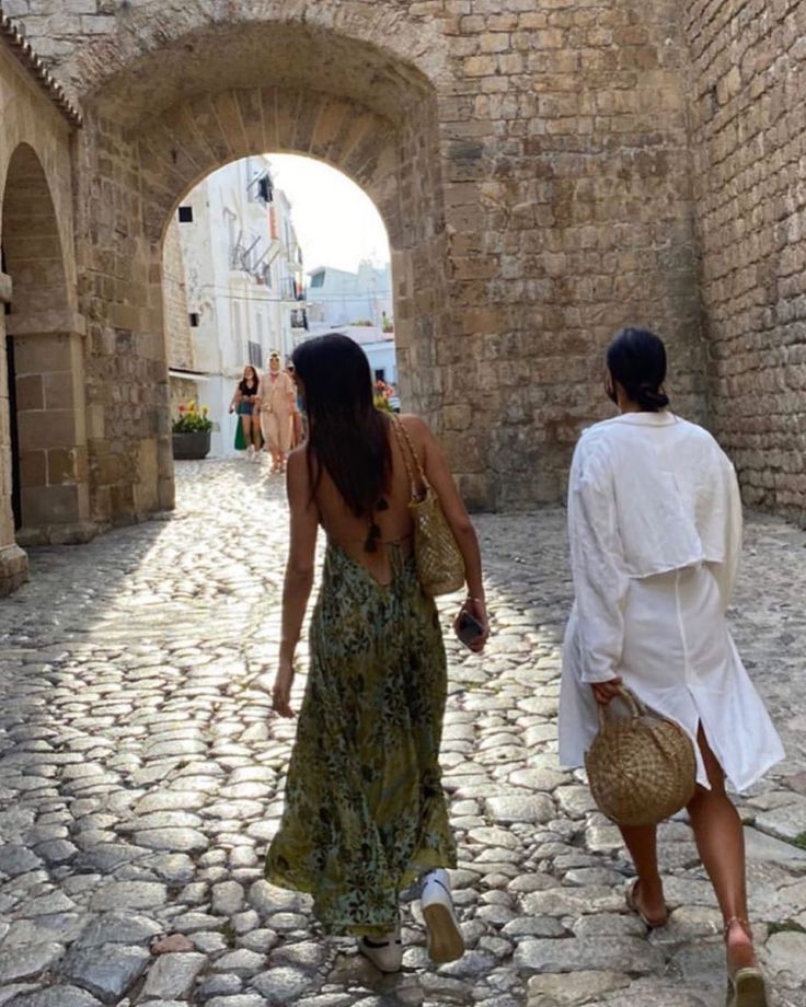 two women walking down a cobblestone street in an alleyway with stone walls