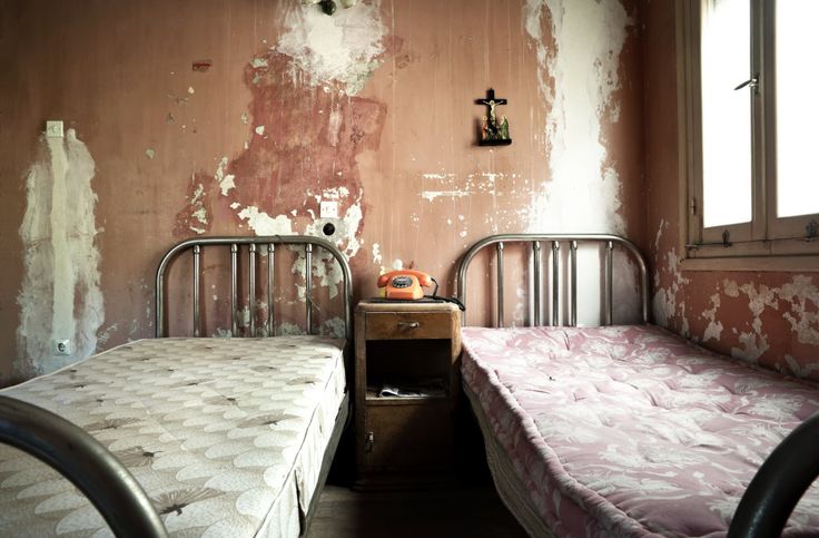 two twin beds in an old room with peeling paint on the walls and wallpaper