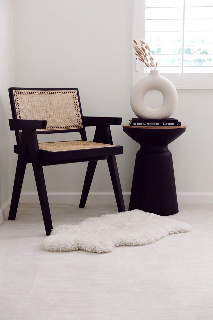 a chair sitting next to a table with a vase on it and a rug in front of it